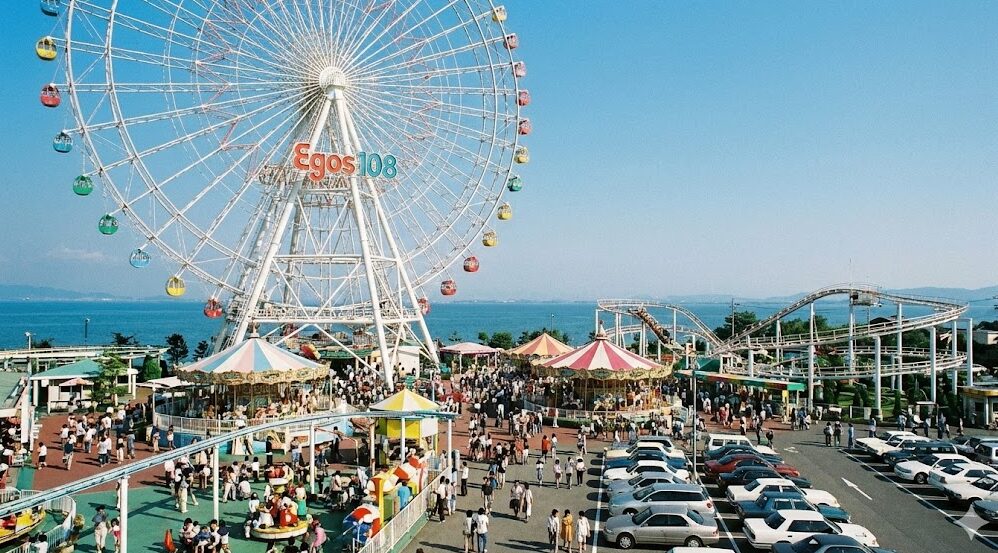 1990年代の最盛期、多くの家族連れで賑わう琵琶湖タワー遊園地の全景。巨大観覧車イーゴス108と琵琶湖が青空の下に広がる。