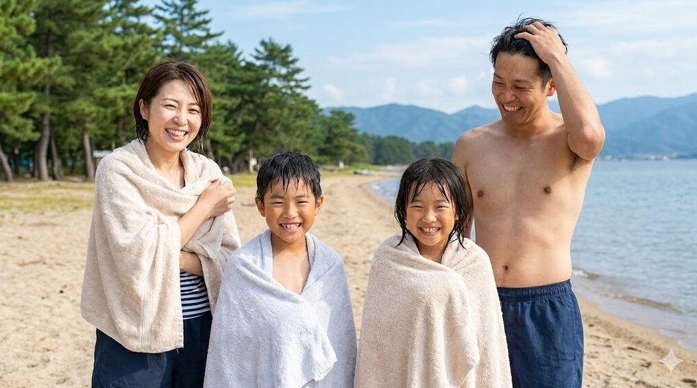 琵琶湖で湖水浴を楽しんだ後、砂浜でタオルを使って体を拭いている笑顔の日本人家族。淡水のため肌がベタつかず、爽快な様子が伝わってくる。
