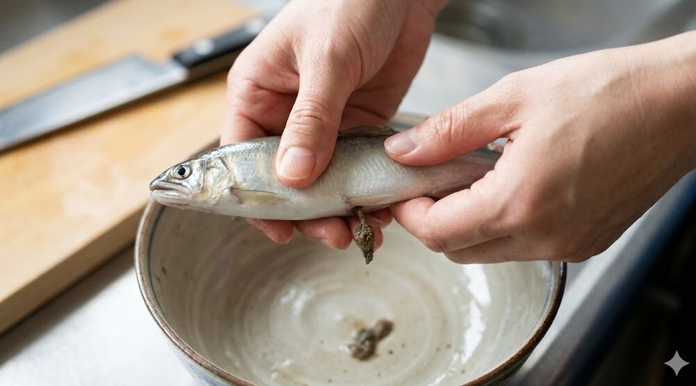 調理前の小鮎のお腹を指で優しく押して、苦味の原因となるフンや砂を出している下処理の手元。