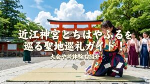 近江神宮の大鳥居の前で、袴姿の女性が競技かるたで札を払う瞬間を捉えた躍動感ある写真。札が宙に舞い、女性は笑顔で手を伸ばしている。背景には、他の袴姿の女性たちが応援しており、青空と緑の木々、赤い鳥居が鮮やか。中央には「近江神宮とちはやふるを巡る聖地巡礼ガイド！」「大会や袴体験も紹介」という白い文字が重ねられている。『ちはやふる』の聖地、近江神宮での巡礼、かるた、袴体験を伝えるアイキャッチ画像。
