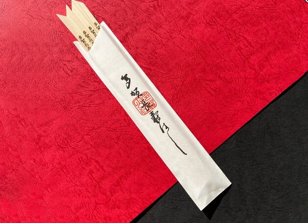 多賀大社の授与品である大きな木製の「お多賀杓子」と、数膳の「多賀長寿はし」が木製の台に並べられている様子。